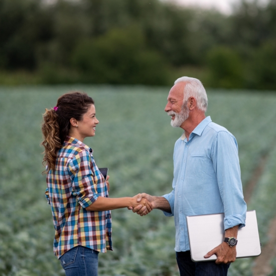 A man and woman shake hands in a field, symbolizing a successful agreement between two individuals.